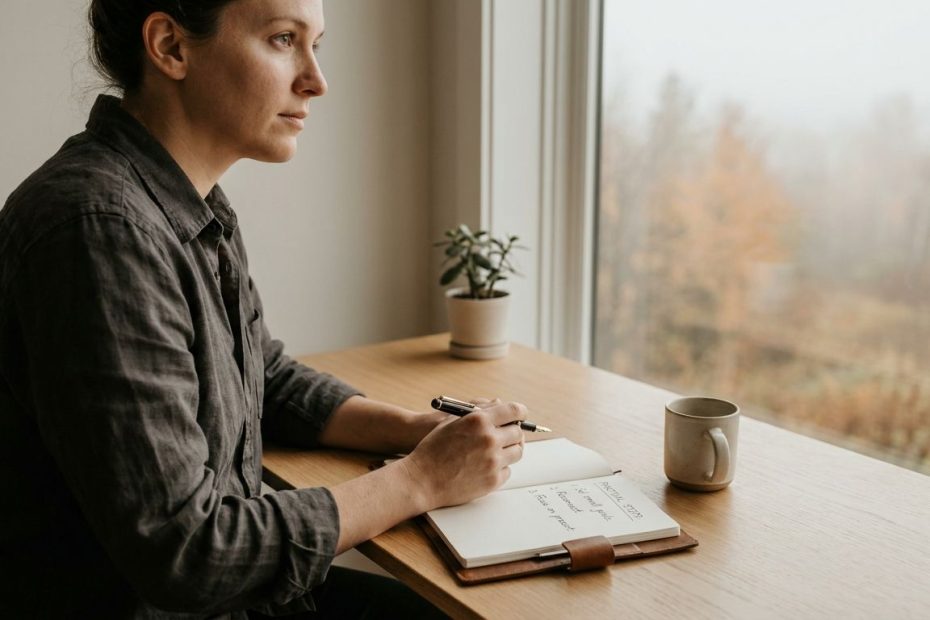 A person journaling beside a window, planning small daily steps to build confidence during uncertainty